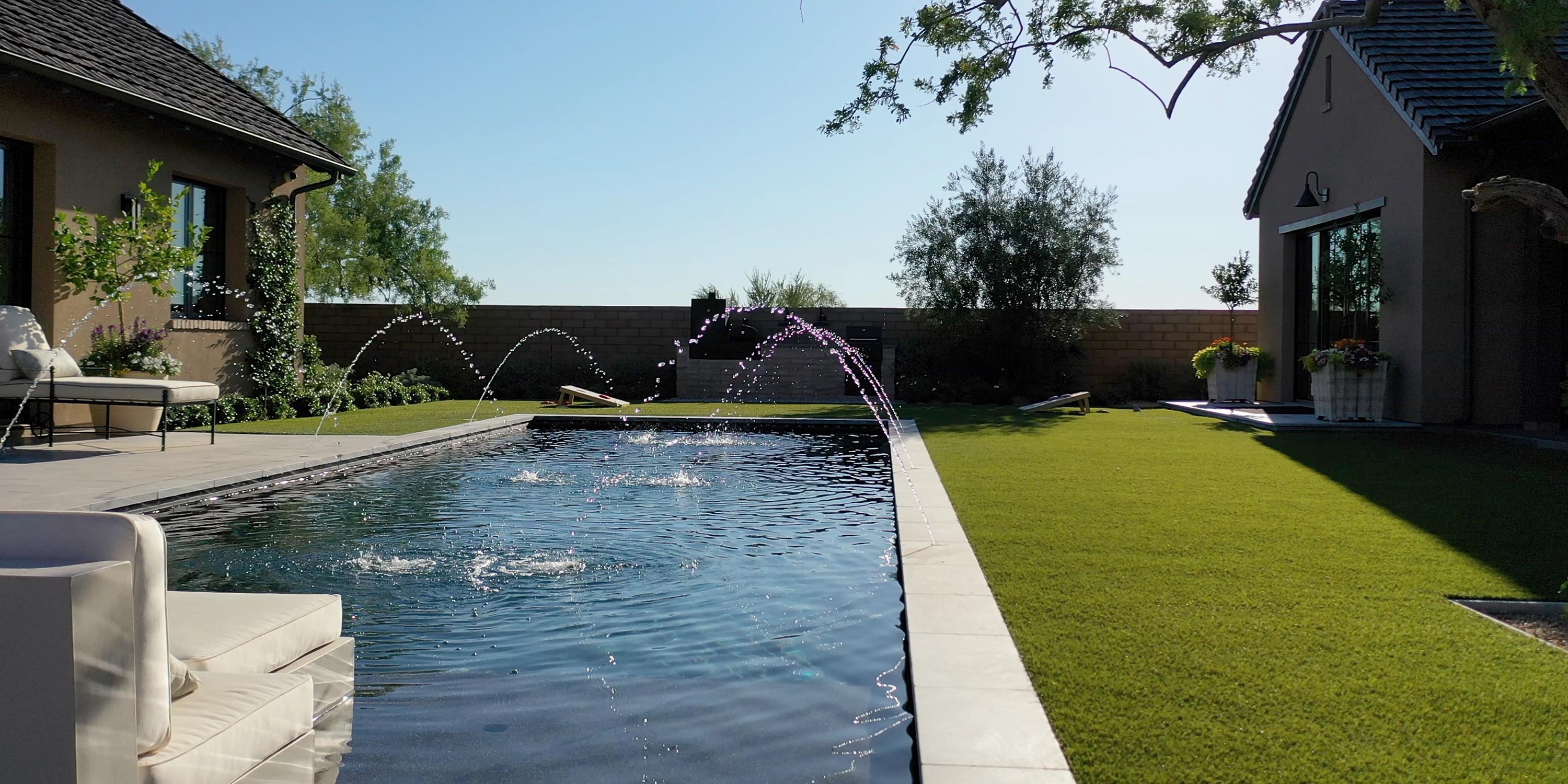 Backyard pool with water fountains and lounge seating under clear skies