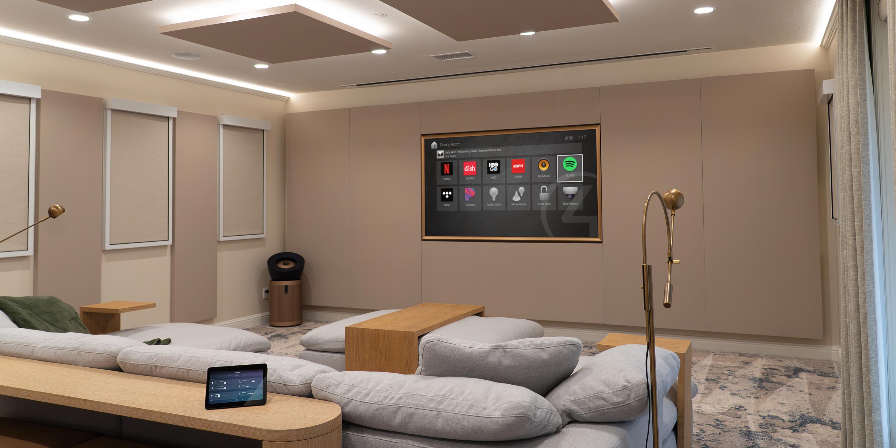Contemporary media room with touch control tablet, plush seating, and smart home interface on screen